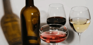 Taças com vinho tinto, branco e rosé representam estudo sobre os efeitos do vinho na saúde bucal por suas propriedades antibacterianas.