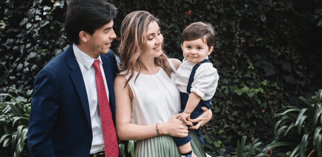 Criança sorridente no colo de mulher ao lado de homem, representando acolhimento familiar após repatriação de bebê brasileiro.