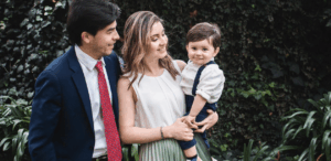 Criança sorridente no colo de mulher ao lado de homem, representando acolhimento familiar após repatriação de bebê brasileiro.