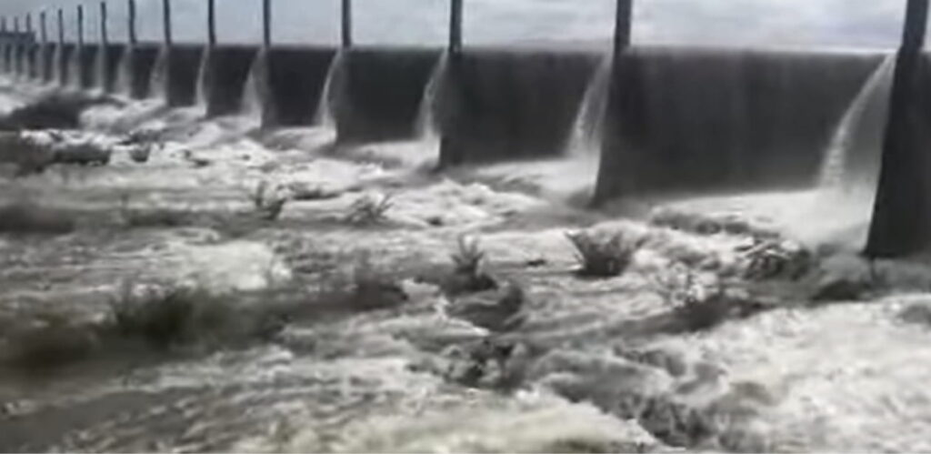 Imagem do Açude Pacajus transbordando, com fortes correntes de água escoando sobre a barragem. O volume intenso reflete o impacto das chuvas na região, contribuindo para a recarga dos reservatórios no Ceará
