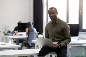 Homem negro em ambiente corporativo, sentado com notebook no colo, representando diversidade em cargos de liderança.