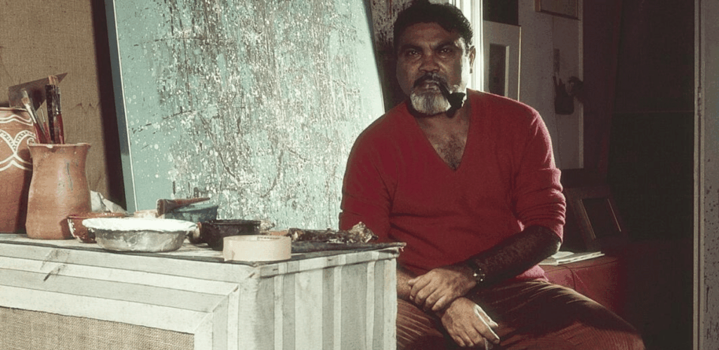 Antonio Bandeira em seu ateliê, com tela abstrata ao fundo e materiais de pintura ao lado.