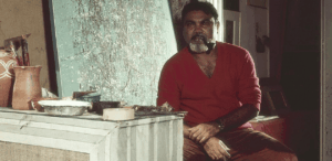 Antonio Bandeira em seu ateliê, com tela abstrata ao fundo e materiais de pintura ao lado.