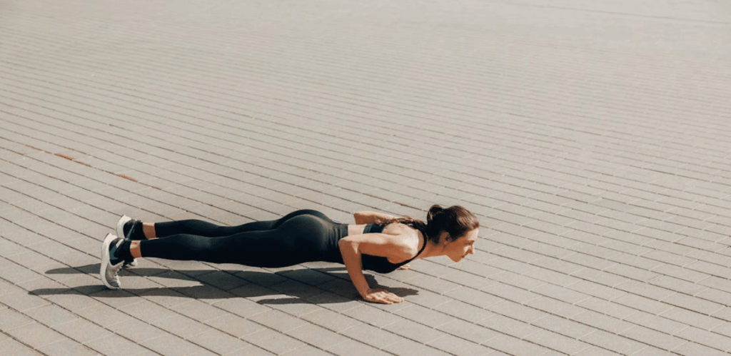 Mulher fazendo flexão ao ar livre como parte de exercícios para emagrecer e melhorar o condicionamento físico.