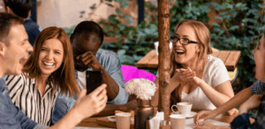 Pessoas sorrindo e conversando em mesa de cafeteria ao ar livre durante o dia, ilustrando a tendência de festas em cafeterias.