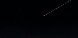 Céu noturno estrelado com rastro luminoso de meteoro cruzando a atmosfera durante uma chuva de meteoros