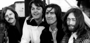 Integrantes da banda The Beatles em foto preto e branco, sorrindo e posando juntos ao ar livre