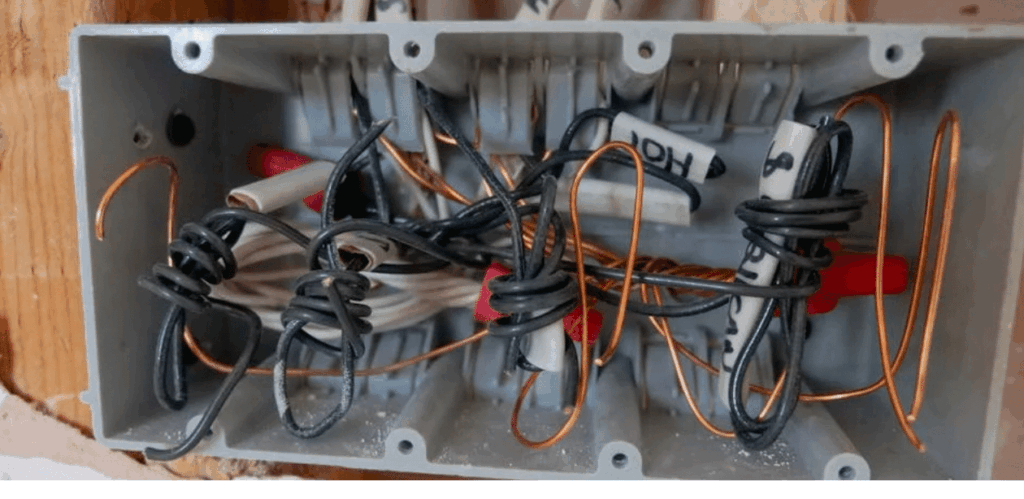 Fiação elétrica desorganizada dentro de caixa de passagem, representando risco de descarga elétrica residencial