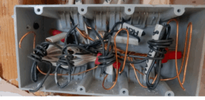 Fiação elétrica desorganizada dentro de caixa de passagem, representando risco de descarga elétrica residencial