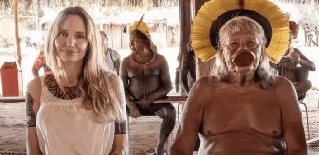 Angelina Jolie sentada ao lado do Cacique Raoni durante visita à Amazônia, em encontro com lideranças indígenas locais.