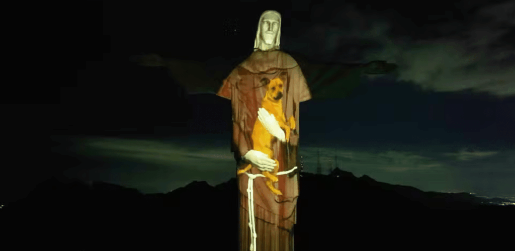 Projeção no Cristo Redentor mostra cão vira-lata caramelo em ação de apoio à adoção responsável de animais.