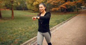 Mulher praticando caminhada para emagrecer em parque arborizado, mantendo ritmo acelerado e monitorando o tempo no relógio