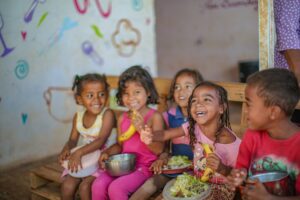 Crianças sorrindo e compartilhando alimentos em ambiente comunitário, representando avanços em segurança alimentar e desenvolvimento humano no Brasil.