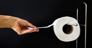 Pessoa puxando papel higiênico corretamente pendurado com a folha voltada para frente