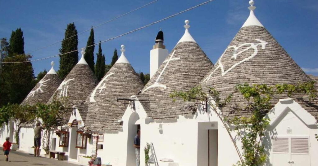 Trulli na Itália com telhado cônico em pedra, ao lado de pátio com área verde e cenário típico de Ostuni, na região de Puglia