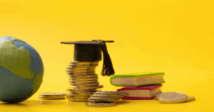 Imagem de moedas espalhadas, capelo e globo sobre fundo amarelo, representando a importância da educação global