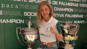 Foto de Leila Pereira em campo, erguendo uma taça com torcedores ao fundo. A influência de Leila Pereira no futebol brasileiro em destaque