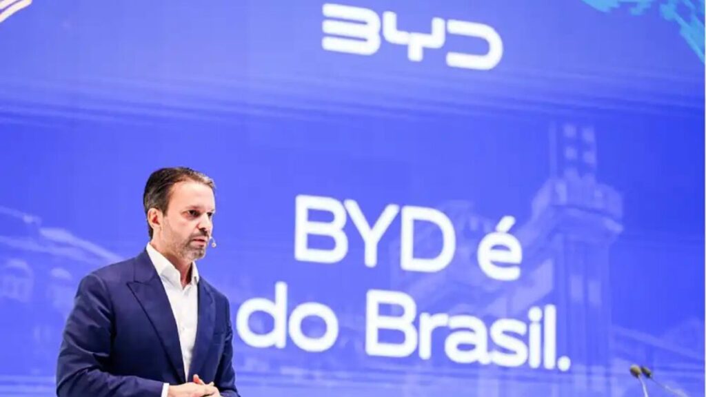 Vagas de emprego na BYD - Homem de terno escuro com microfone de lapela fala em frente a um telão azul com o texto “BYD é do Brasil”; trata-se de Alexandre Baldy, executivo da montadora.