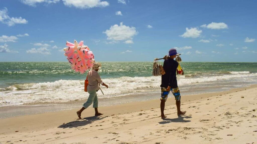 Empreendedores ambulantes na praia simbolizando o trabalho informal e o apoio do Sebrae Ceará na inclusão produtiva.