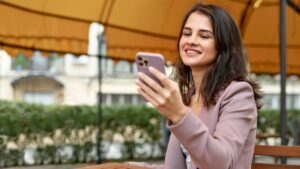 Mulher segura o smartphone em um café ao ar livre; imagem ilustrativa do alerta do whatsapp e das novas dicas de segurança.