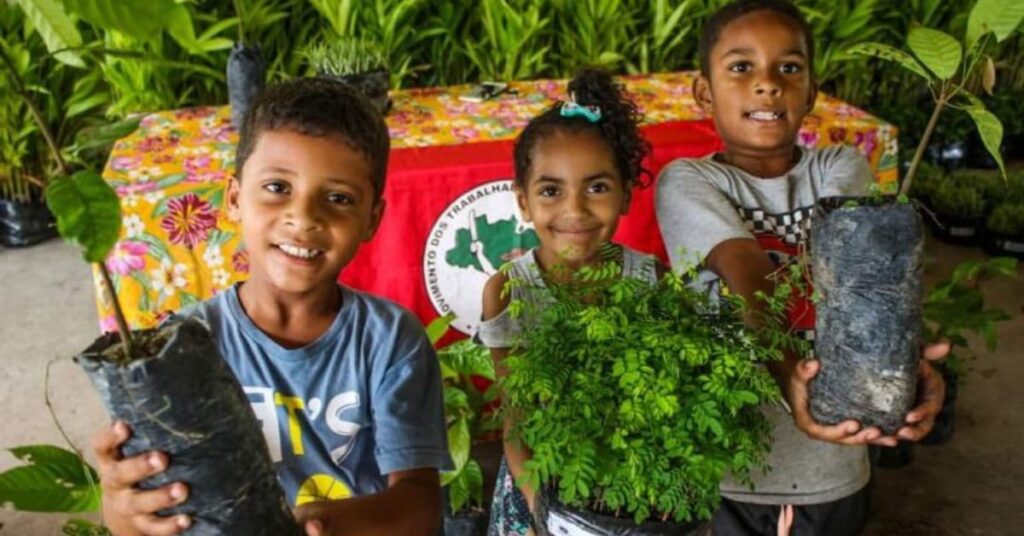 Crianças seguram mudas durante ação de reflorestamento popular no Brasil do MST \