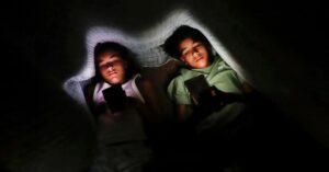 : duas crianças usam celulares no escuro, representando o desafio da supervisão familiar online.