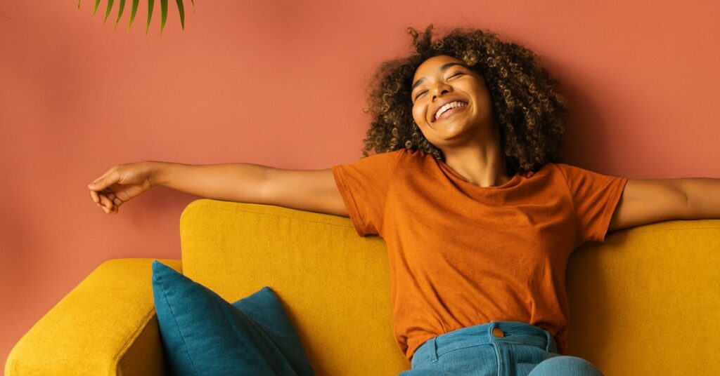 Mulher sorridente relaxando no sofá após aprovação em programa habitacional para classe média.”