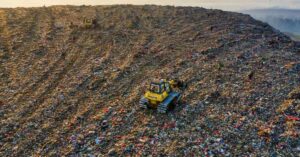 Aterro sanitário com toneladas de resíduos têxteis e máquinas em operação, simbolizando a urgência da reciclagem na moda na Europa.