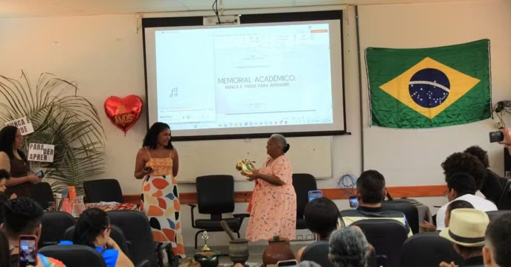 Idosa apresenta o TCC na UFNT segurando saxofone ao lado da orientadora, durante defesa de Maria de Fátima TCC