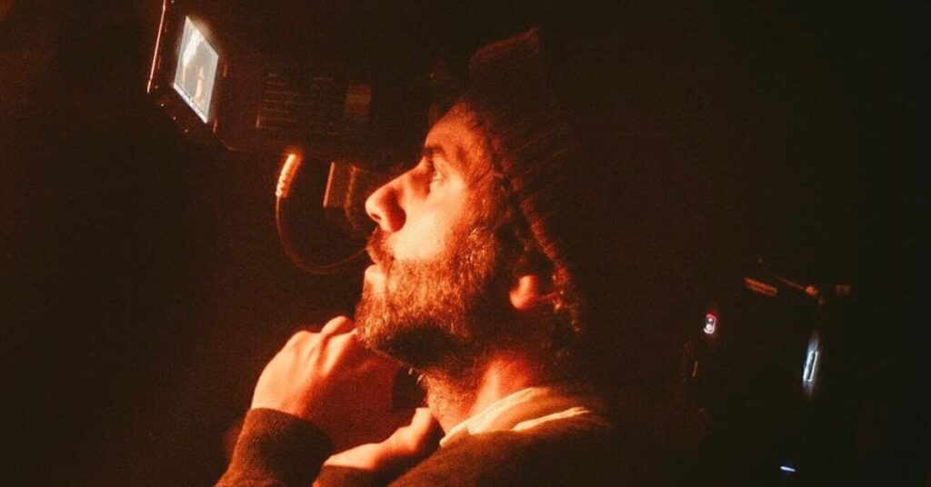 Adolpho Veloso no Oscar 2026 segurando uma câmera em ambiente escuro